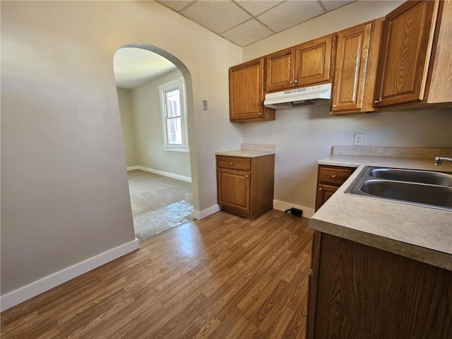 kitchen featuring arched walkways, baseboards, a sink, and under cabinet range hood