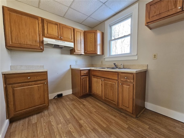 kitchen featuring brown cabinets, a sink, wood finished floors, under cabinet range hood, and baseboards