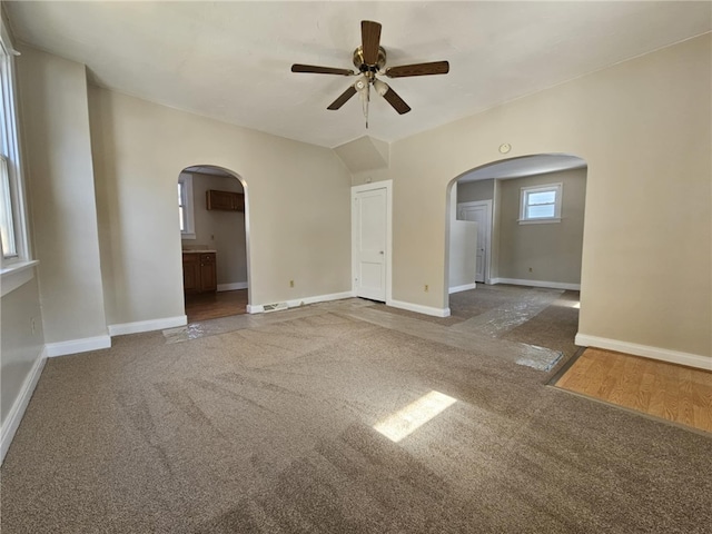 unfurnished room featuring carpet floors, arched walkways, lofted ceiling, a ceiling fan, and baseboards