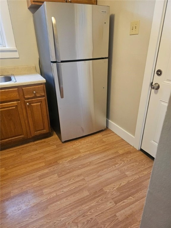 kitchen featuring baseboards, light countertops, freestanding refrigerator, brown cabinets, and light wood finished floors