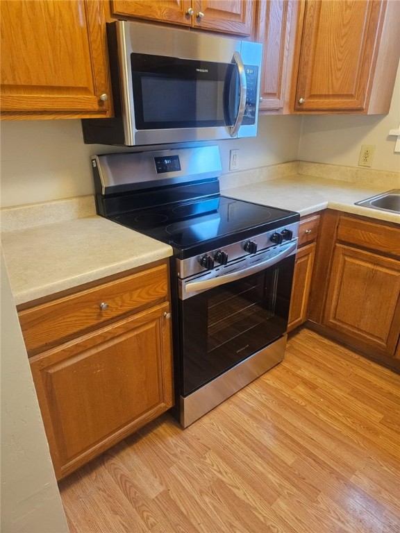 kitchen with stainless steel appliances, light countertops, brown cabinets, and light wood-style floors