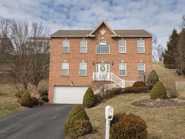 colonial home with driveway, brick siding, and an attached garage