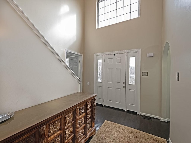 foyer featuring a towering ceiling, baseboards, arched walkways, and dark wood-style flooring