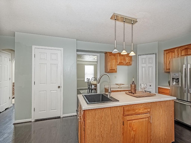 kitchen with stainless steel fridge, dark wood-style floors, brown cabinets, light countertops, and a sink