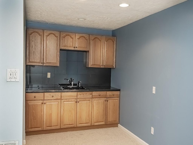 kitchen featuring a textured ceiling, a sink, baseboards, tasteful backsplash, and dark countertops