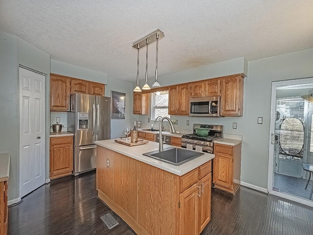 kitchen with a center island with sink, dark wood-style floors, stainless steel appliances, light countertops, and a sink