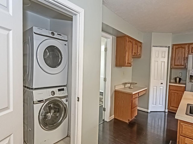 washroom with dark wood-type flooring, a textured ceiling, stacked washing maching and dryer, laundry area, and baseboards