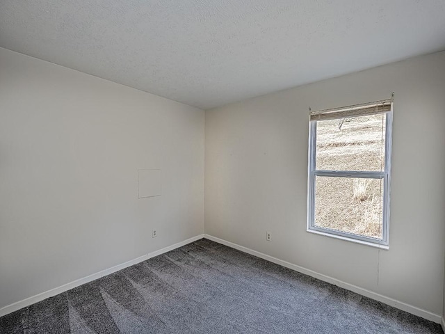 spare room with a textured ceiling, dark colored carpet, plenty of natural light, and baseboards