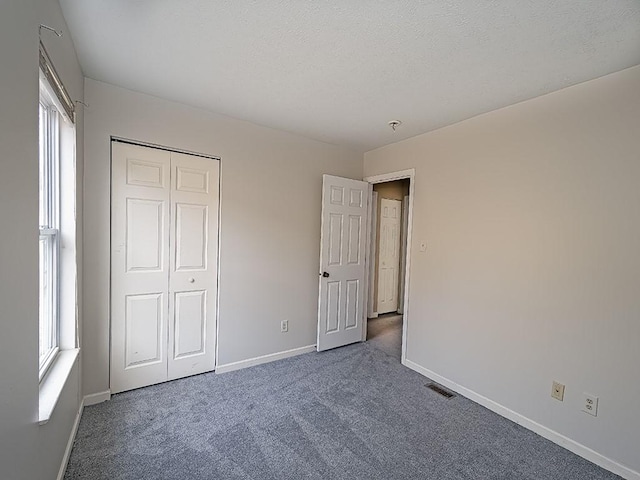 unfurnished bedroom featuring carpet floors, visible vents, a textured ceiling, and baseboards