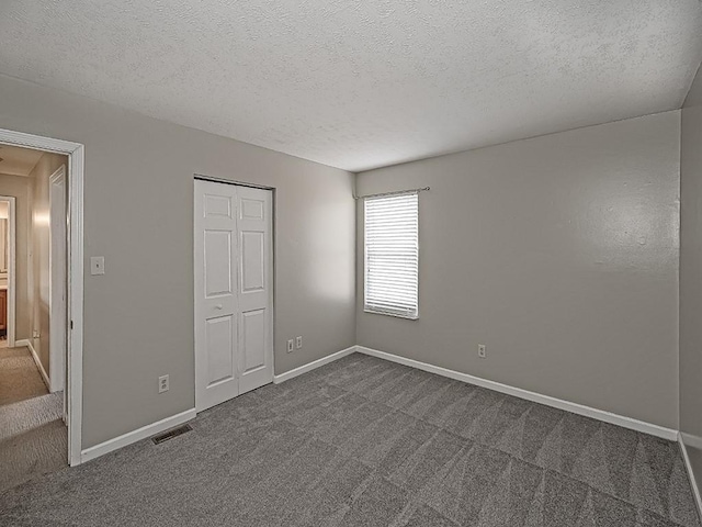 unfurnished bedroom featuring a textured ceiling, a closet, visible vents, dark colored carpet, and baseboards