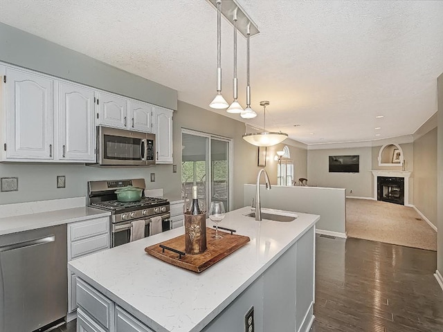 kitchen with white cabinetry, appliances with stainless steel finishes, a kitchen island with sink, a sink, and hanging light fixtures