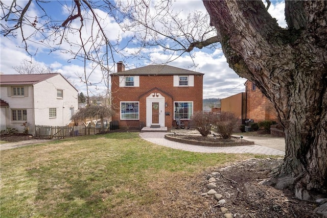 view of front facade featuring brick siding, a chimney, a front lawn, and fence