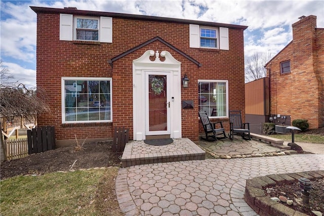 view of front facade featuring brick siding, a patio area, and fence