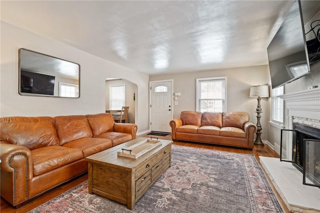 living room with arched walkways, a premium fireplace, wood finished floors, and baseboards