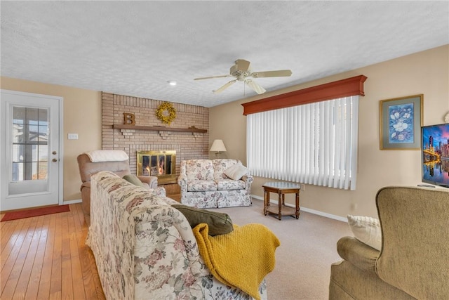 living room featuring a brick fireplace, a ceiling fan, baseboards, and a textured ceiling