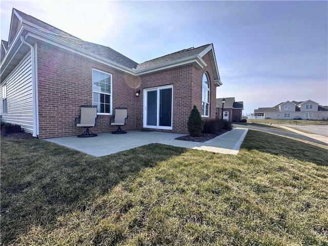 rear view of property featuring a yard, brick siding, and a patio