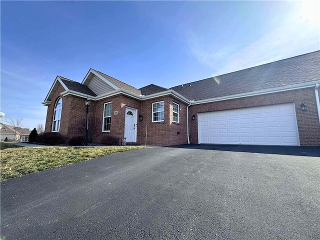 ranch-style home with a garage, brick siding, driveway, and roof with shingles