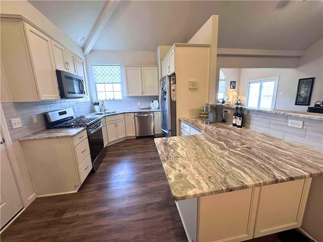 kitchen with appliances with stainless steel finishes, backsplash, a peninsula, vaulted ceiling with beams, and a sink