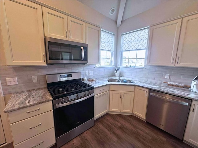 kitchen with appliances with stainless steel finishes, dark wood-style flooring, a sink, vaulted ceiling, and backsplash