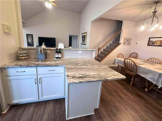 kitchen with a peninsula, dark wood-type flooring, light stone countertops, and white cabinets