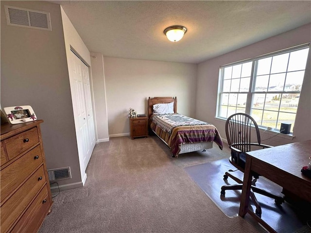 carpeted bedroom with a textured ceiling, a closet, visible vents, and baseboards