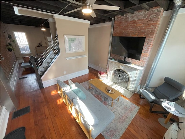 living room featuring hardwood / wood-style flooring, a large fireplace, visible vents, a ceiling fan, and stairs