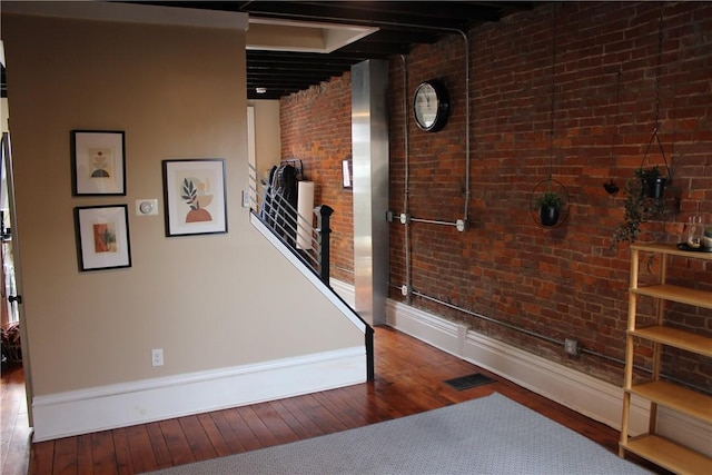 hall featuring wood-type flooring, brick wall, and baseboards