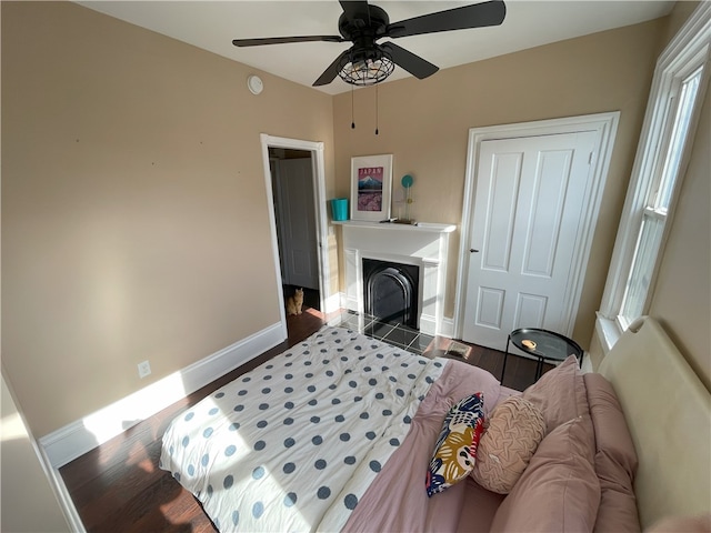 bedroom with ceiling fan, a fireplace, wood finished floors, and baseboards