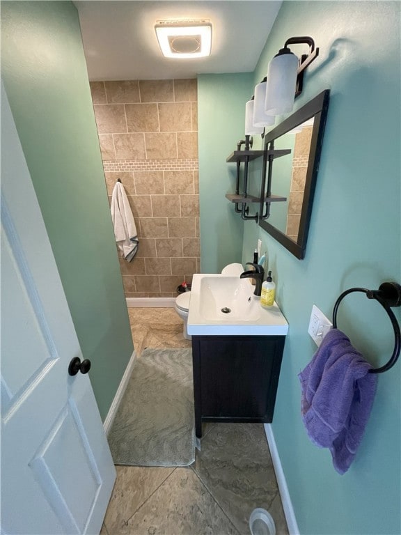 bathroom featuring toilet, tiled shower, vanity, and baseboards