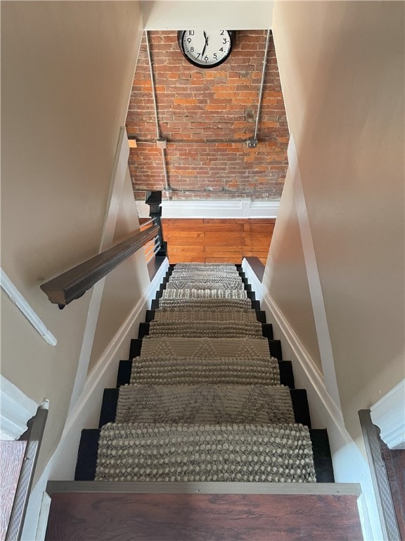 staircase with baseboards, brick wall, and wood finished floors