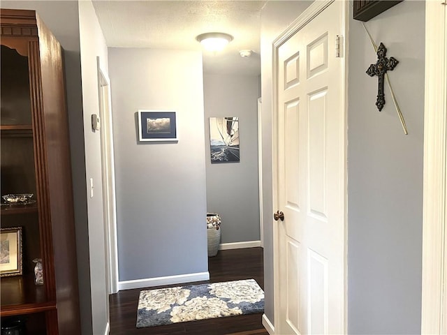 hallway featuring a textured ceiling, dark wood-type flooring, and baseboards