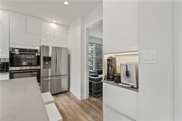 kitchen with light wood finished floors, modern cabinets, stainless steel appliances, white cabinetry, and recessed lighting