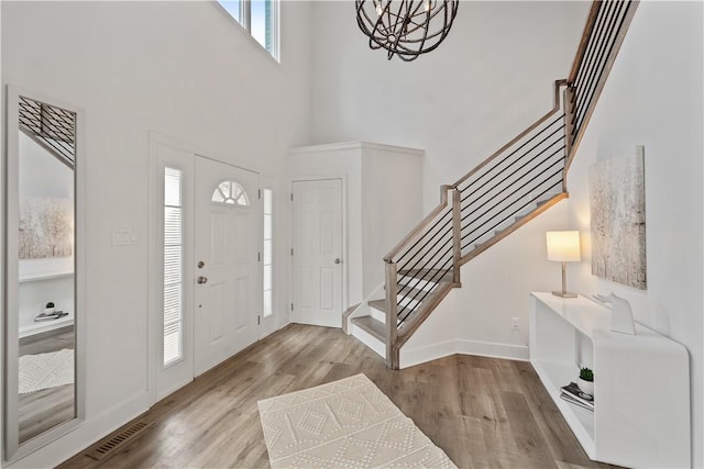 foyer entrance with visible vents, stairway, an inviting chandelier, wood finished floors, and baseboards