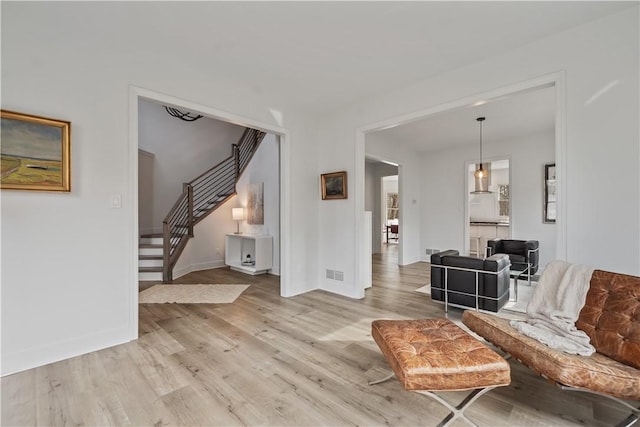 living room featuring light wood-style flooring, visible vents, stairway, and baseboards