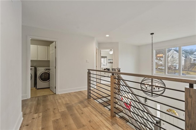 hallway with a notable chandelier, washing machine and dryer, an upstairs landing, light wood-type flooring, and baseboards