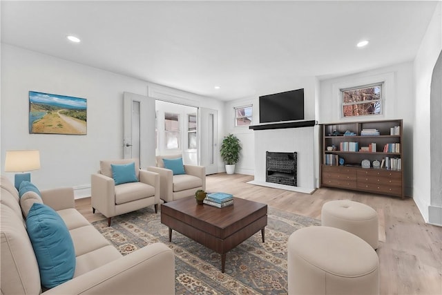 living area featuring a fireplace with flush hearth, baseboards, wood finished floors, and recessed lighting