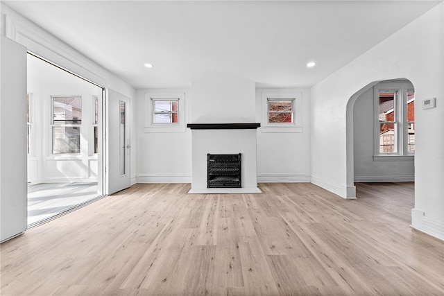 unfurnished living room with light wood-style floors, baseboards, plenty of natural light, and a fireplace with flush hearth