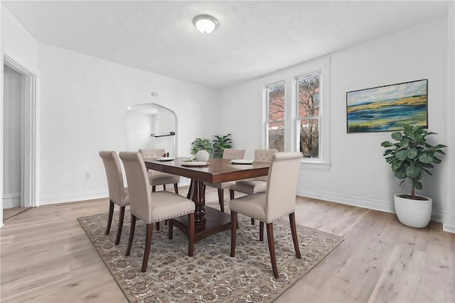 dining area with light wood-style floors, baseboards, and arched walkways