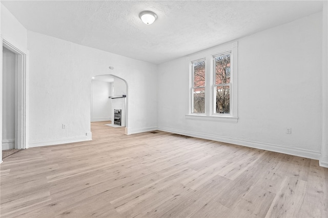 unfurnished living room featuring baseboards, light wood-style flooring, arched walkways, and a textured ceiling