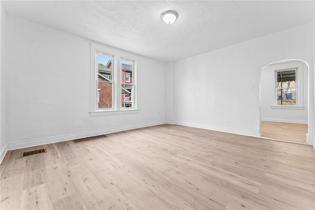 unfurnished room with arched walkways, light wood-type flooring, visible vents, and baseboards