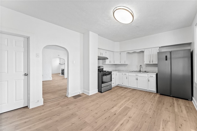 kitchen with arched walkways, black range with gas cooktop, under cabinet range hood, light countertops, and freestanding refrigerator