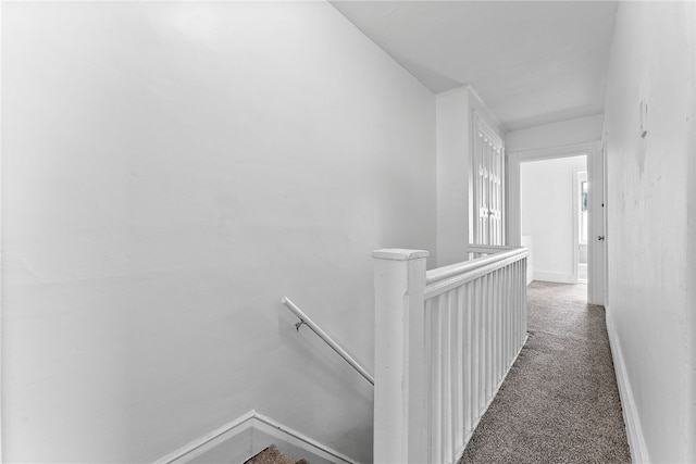 hallway with carpet, baseboards, and an upstairs landing