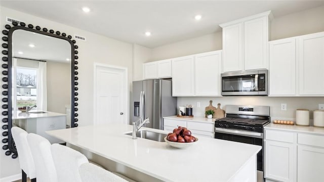 kitchen with a kitchen island with sink, light countertops, white cabinets, a sink, and appliances with stainless steel finishes