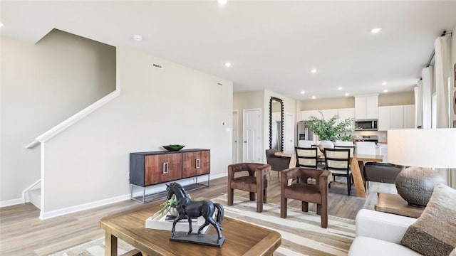 living area with light wood-style flooring, recessed lighting, baseboards, visible vents, and stairway