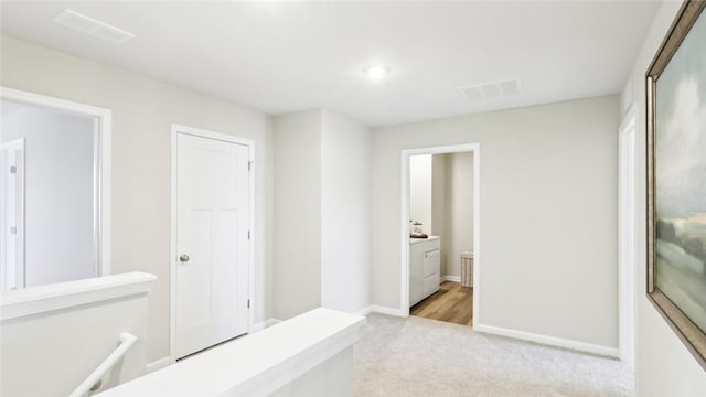 hallway featuring visible vents, baseboards, and light carpet