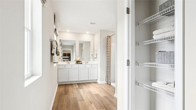 interior space featuring double vanity, a shower with curtain, baseboards, and wood finished floors
