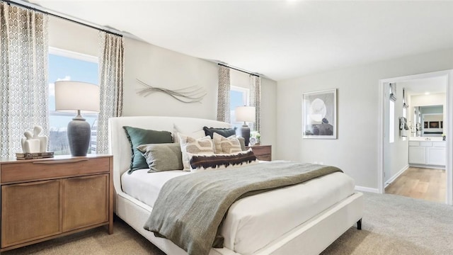 bedroom featuring baseboards, connected bathroom, and light carpet