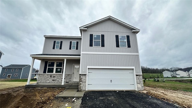 view of front of property featuring stone siding, driveway, covered porch, and a garage