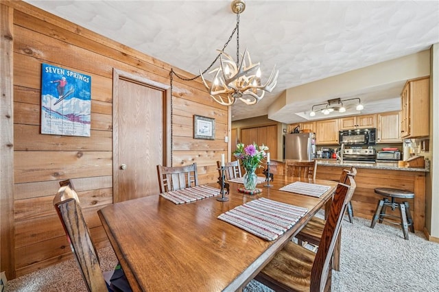 dining room featuring light carpet, a toaster, wood walls, and a notable chandelier