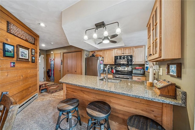 kitchen featuring light stone counters, appliances with stainless steel finishes, glass insert cabinets, a sink, and a peninsula